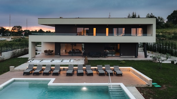 Una casa moderna de dos pisos con piscina, mobiliario exterior y un jardín bien cuidado.