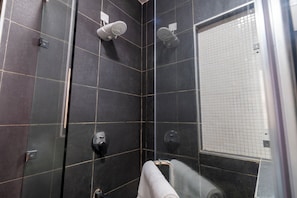 Un baño moderno con baldosas oscuras, cabina de ducha de vidrio y un toallero visible.