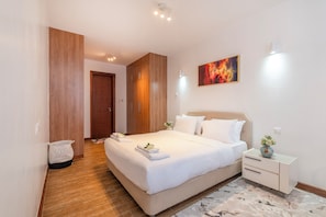 Una habitación de hotel moderna con una cama grande, mesitas de noche, un armario de madera y un cuadro en la pared.