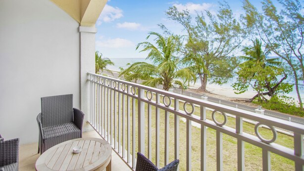 A balcony with wicker furniture and a view of the beach and palm trees. - NEW Gated Beach front Condo (Nassau)