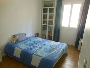 A bedroom with a bed, a bookshelf, and a window with curtains.