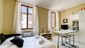 Una habitación de hotel con cama, escritorio, televisor y ventana con cortinas.