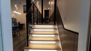 Eine Treppe mit Holzdielen und schwarzen Geländern, die zu einem Raum mit Schreibtisch und Stühlen führt.