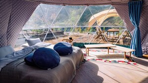 Une tente confortable et bien éclairée, avec un lit, des oreillers et une petite table.