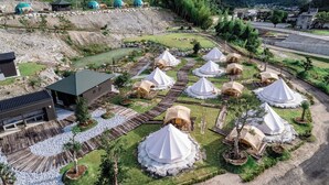 Un terrain de camping où des yourtes sont disposées en cercle, entourées d’une terrasse en bois et d’un petit étang.