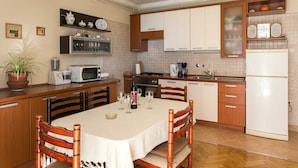 A kitchen with wooden cabinets, a dining table with chairs, a microwave, a stove, and a refrigerator. - Apartments Miljan Popovic (Konavle)