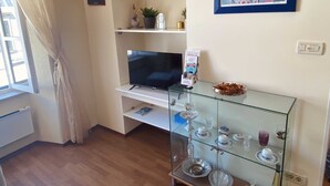 A living room with a TV, glass display case with dishes, a framed picture, and a window with curtains.