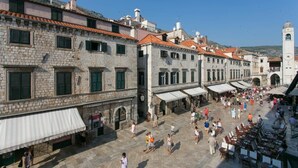 A historic stone building with a clock tower, outdoor seating, and a bustling square.