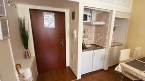 A compact kitchen with a wooden door, white cabinets, a microwave, and a small dining area with a table and chairs.