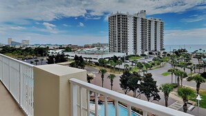 A high-rise hotel with a pool area, surrounded by palm trees and a clear sky. - Ariel Dunes #510 | Gulf Side Condo, Amazing Water Views + Resort Amenities! (Miramar Beach)