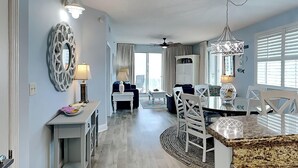 A spacious living area with a dining table, chairs, and a kitchen area with a counter and cabinets. - Ariel Dunes #510 | Gulf Side Condo, Amazing Water Views + Resort Amenities! (Miramar Beach)