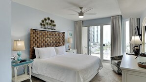A hotel room with a large bed, a ceiling fan, a view of the city through the window, and a balcony with a chair. - Ariel Dunes #510 | Gulf Side Condo, Amazing Water Views + Resort Amenities! (Miramar Beach)