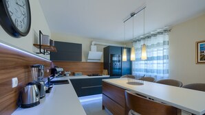 A compact kitchen with a white countertop, a built-in stove, and a coffee machine. There is a dining area with a wooden table and chairs. - Brand new apartment Excellence with 3 bedrooms and 3 bathrooms (Pula)