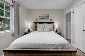 A bedroom with a bed, two bedside tables, a window with curtains, and a door. - Captain and Crew at Seaside Beach (Seaside)
