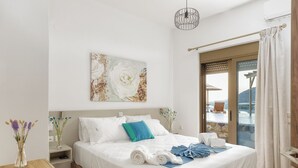 A modern hotel room with a large bed, a view of the outdoors, and a wooden table with a vase of flowers. - 2 Bedroom Villa in Mediterranean View Villas in Makri gialos (Makry Gialos)