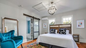 Une chambre à coucher avec un grand lit, une chaise bleue, un tapis coloré et une vue sur l’extérieur par une fenêtre.