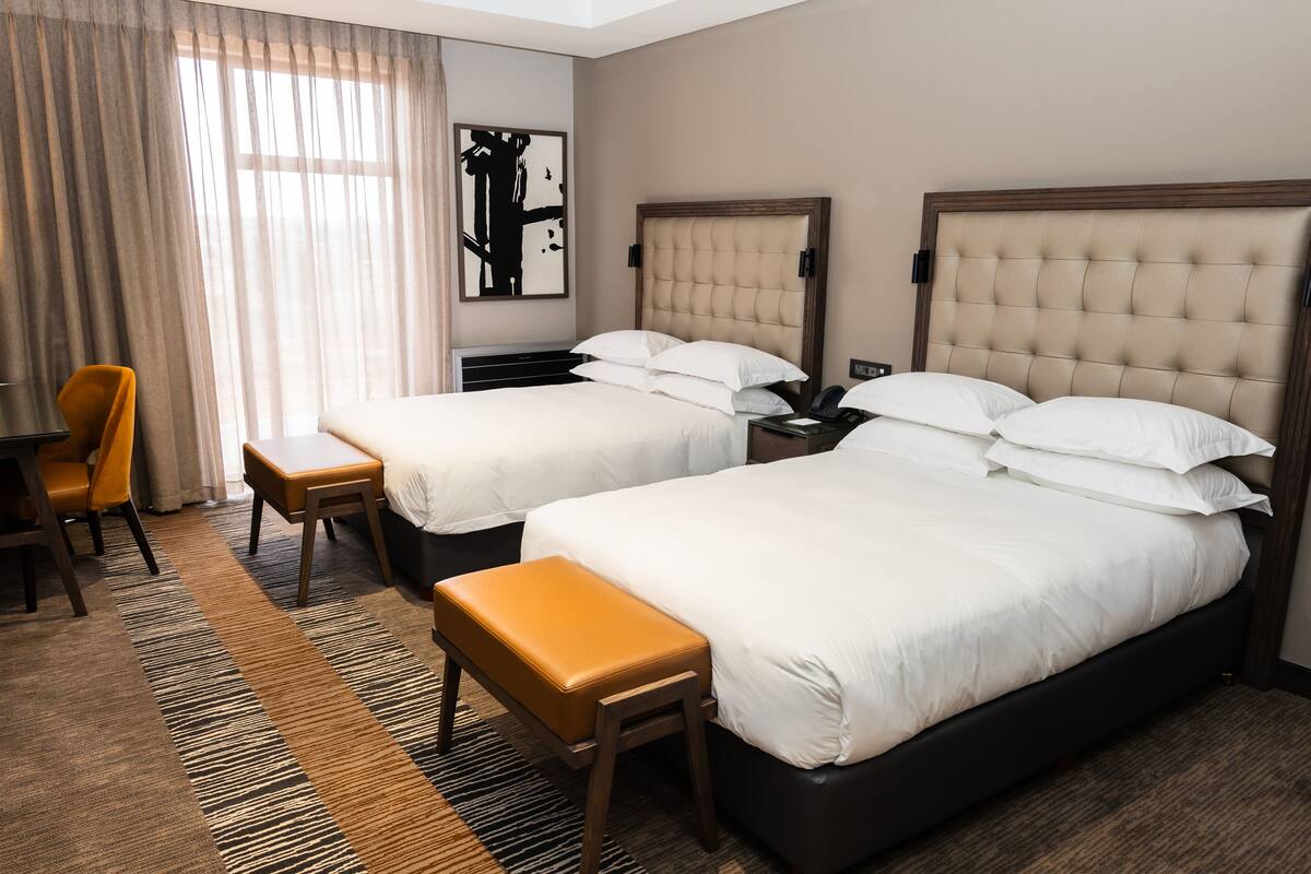 A hotel room with two beds, a desk, and a chair.