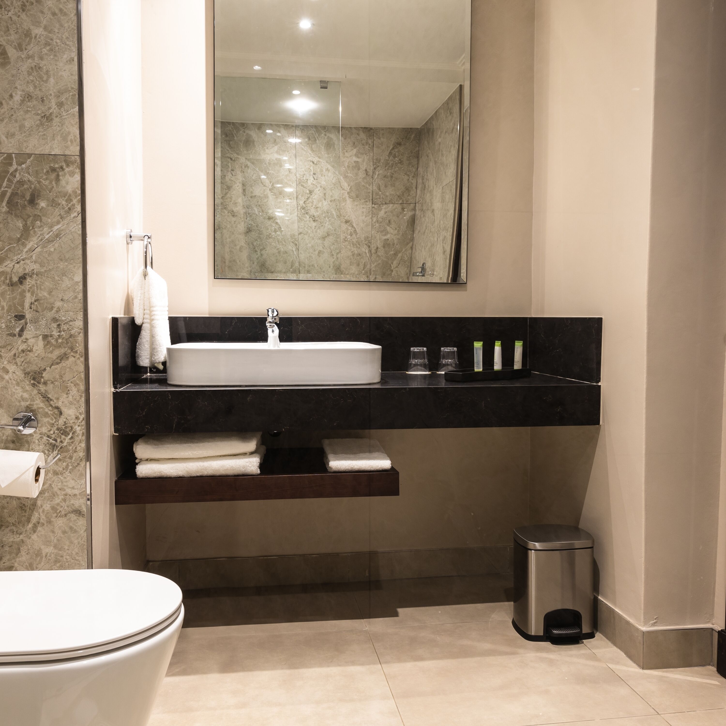 Un bagno moderno con lavabo in marmo, uno specchio sopra il lavabo, un water e un cestino.