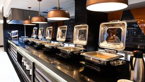 A buffet setup with multiple serving stations, stainless steel serving trays, and overhead pendant lighting. - Premier Hotel Thohoyandou (Thohoyandou)