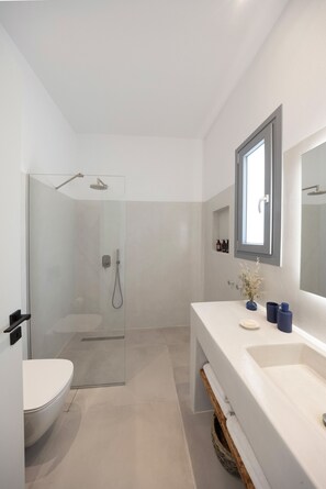 Un baño moderno con ducha de vidrio, un lavabo blanco y un espejo encima.
