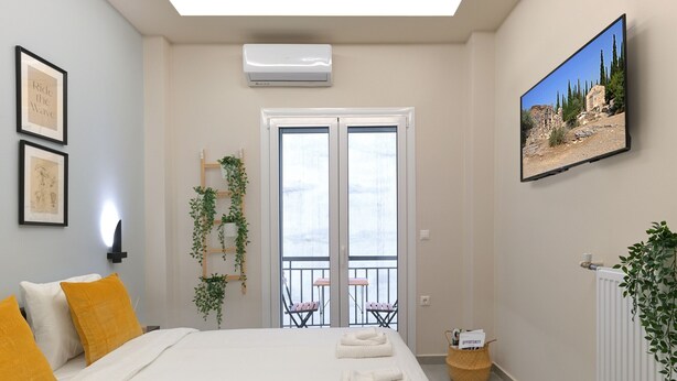 Et soveværelse med seng, to puder, fastgjort klimaanlæg, vægmonteret TV, balkon med stol og en radiator.