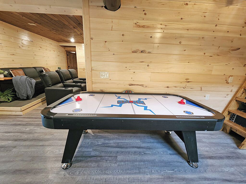 Une table de baby-foot dans une pièce aux murs en bois et où se trouve un canapé.