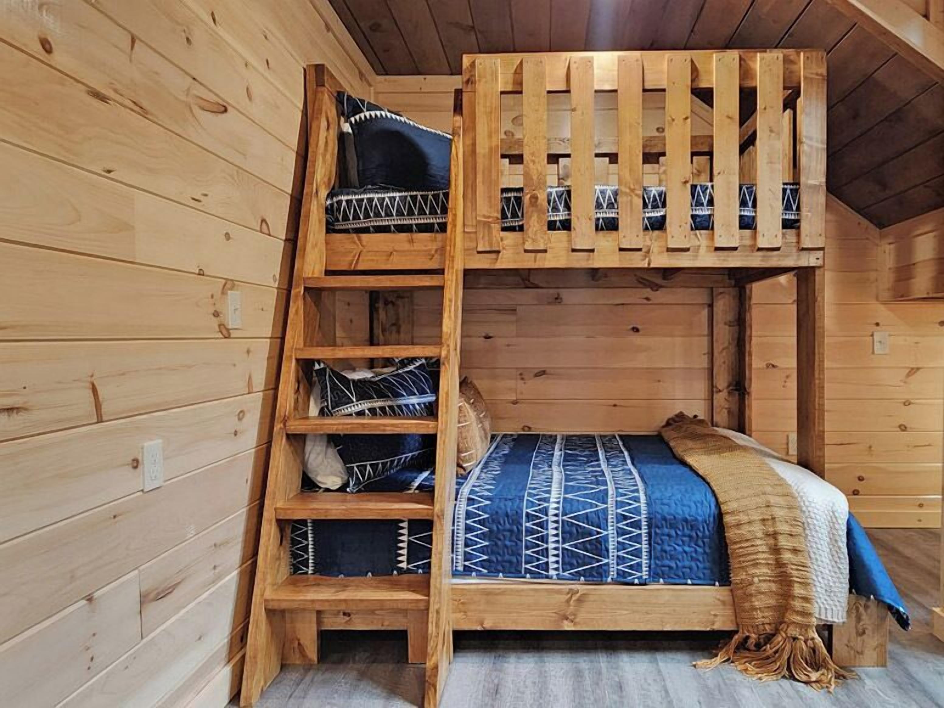 A bunk bed with a ladder, a blue patterned bedspread, and a beige blanket.