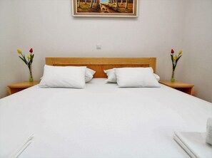A neatly made bed with white linens and pillows, a wooden headboard, and two nightstands with vases of flowers. - Adria View, Apartment Ina with pool (Makarska)