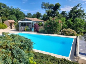 Une piscine dotée d’un espace de repos couvert et entourée d’une végétation luxuriante.