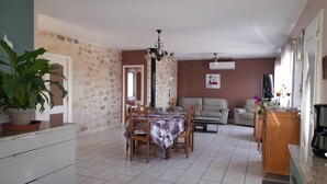 A spacious living area with a dining table, sofas, and a stone wall. - Maison de Plain Pied à la Campagne Entre Bergerac et Villeneuve SUR LOT (Cancon)