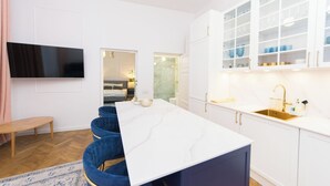 Une cuisine moderne avec des meubles blancs, un plan de travail en marbre et un évier doré. On y trouve également un coin repas avec une table blanche et des chaises bleues.
