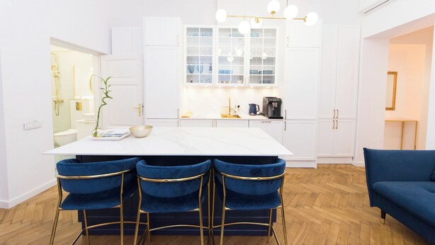 Une cuisine moderne avec des meubles blancs, un plan de travail en marbre et un îlot central doté de tabourets de bar.