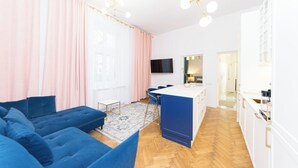 Un salon moderne avec un canapé bleu, une petite table blanche et un téléviseur fixé au mur.