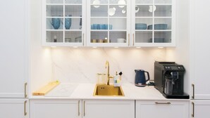 Une cuisine moderne avec des meubles blancs, un plan de travail en marbre, une machine à café et des meubles hauts à façade vitrée où sont exposées de la vaisselle et des verres.