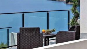 A balcony with wicker furniture, a fruit bowl, and a view of a lake and distant buildings. - Villa Legero with pool (Drašnice)