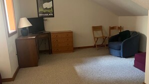 A small, dimly lit room with a sloped ceiling, a television, a wooden cabinet, a blue chair, and a poster on the wall. - Roomy ski condo next to Mt. Snow, on the mover bus, with hot tub and sauna! (Dover)