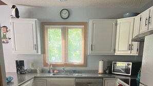 A kitchen with white cabinets, a microwave, a dishwasher, and a window with blinds. - Roomy ski condo next to Mt. Snow, on the mover bus, with hot tub and sauna! (Dover)