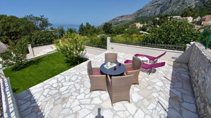 A patio with wicker furniture and a table, overlooking a mountainous landscape and a body of water. - Villa Silencio with pool (Tucepi)