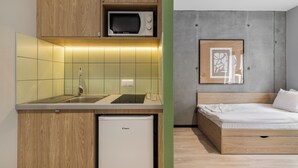 A compact kitchen with a microwave, sink, and refrigerator, and a bed with a wooden headboard and a framed picture on the wall. - NextDoor Apartments (Kraków)