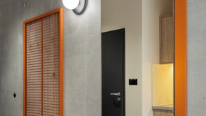 A modern interior with a concrete wall, a wooden cabinet, and a mirror reflecting a room with a door and a light fixture. - NextDoor Apartments (Kraków)