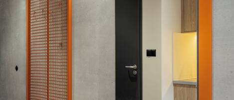 A modern interior with a concrete wall, a wooden cabinet, and a mirror reflecting a room with a door and a light fixture.
