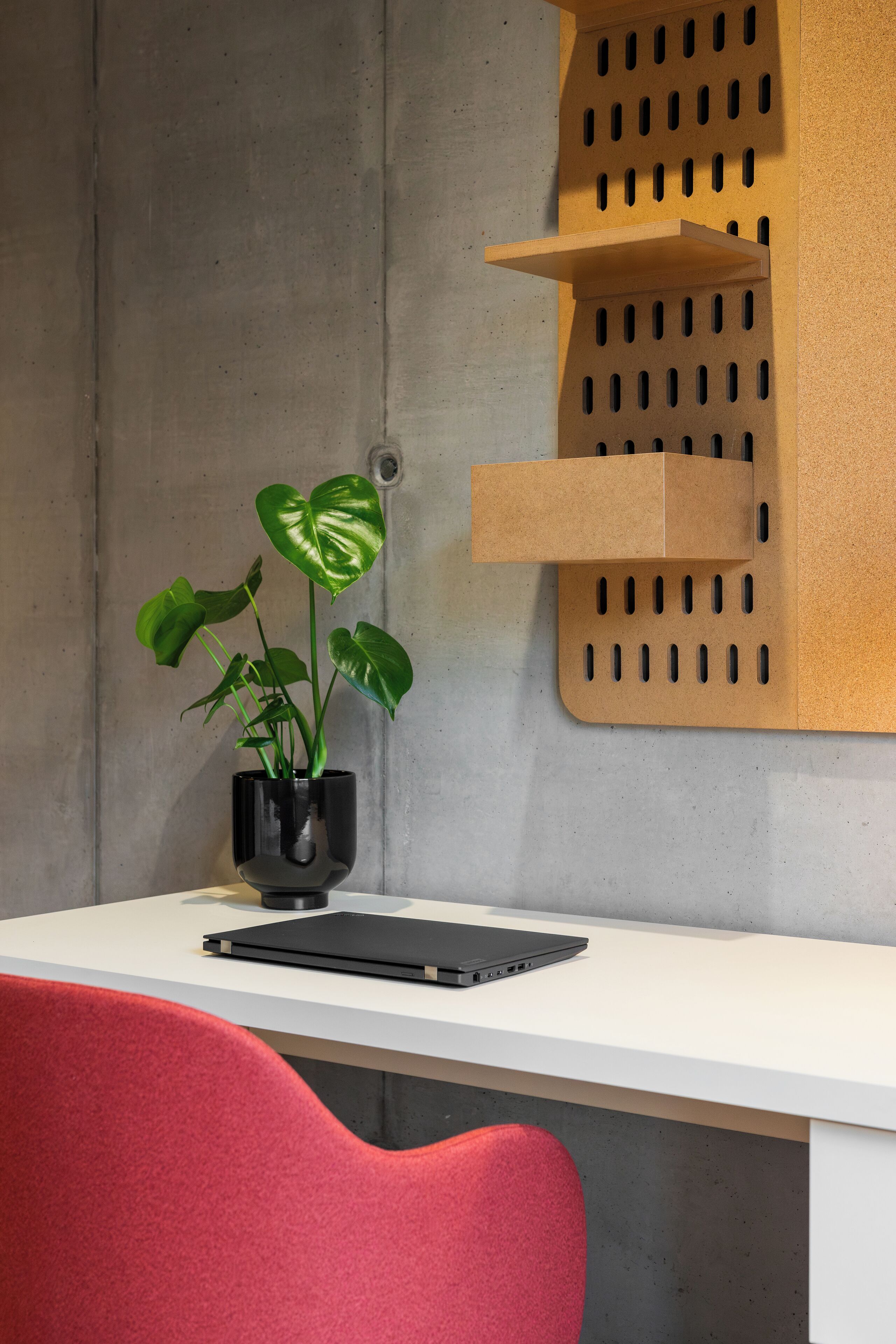 A workspace with a white desk, a black laptop, a red chair, and a potted plant.