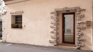 Un bâtiment à la façade beige, avec une entrée encadrée de pierres, une petite fenêtre ornée d’une plante et une boîte aux lettres.