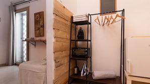 A compact room with a bed, a wooden wall, a black shelf with a kettle and an iron, and a white refrigerator. - Iknos Suites by Wonderful Italy - Sunflower (Olbia)
