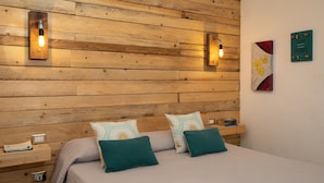 A bedroom with a wooden headboard, two bedside tables, a bed with teal and white bedding, and wall-mounted lights. - Iknos Suites by Wonderful Italy - Sunflower (Olbia)