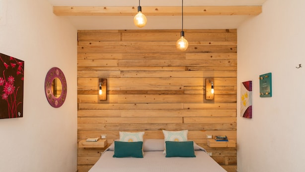 A bedroom with a wooden headboard, two bedside tables, and a bed with teal pillows. - Iknos Suites by Wonderful Italy - Sunflower (Olbia)