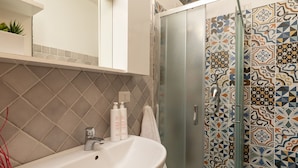 A bathroom with a white sink, a glass shower enclosure, and patterned tiles. - Iknos Suites by Wonderful Italy - Sunflower (Olbia)