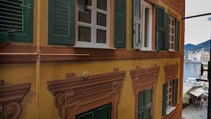 Um edifício com persianas verdes, varanda e vista para um corpo de água e edifícios ao longe.
