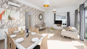 Un salon moderne comprenant un coin repas, un ensemble de canapés, un téléviseur et une table basse en verre.