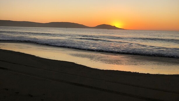 A beach at sunset with calm waves and a clear sky.